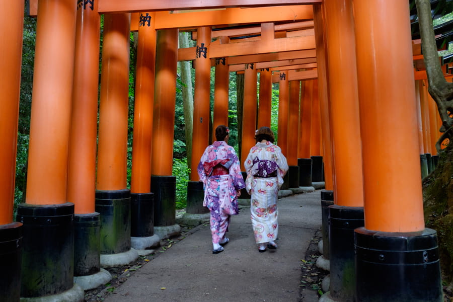 Dos personas con trajes tradicionales japoneses caminando por el sendero Torii del templo Fushimi Inari