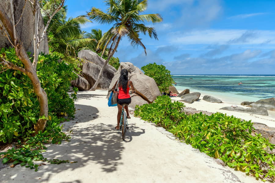 Una ciclista recorre en bicicleta un camino de arena en una playa tropical de la isla de La Digue